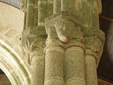 Gros plan sur un chapiteau où figure un masque humain. L'inscription court sur deux faces du tailloir.