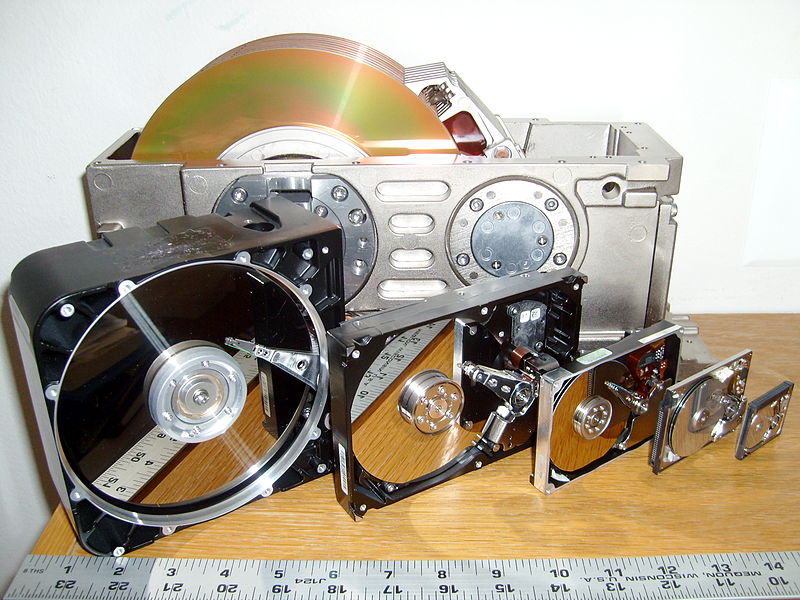 Six hard disk drives with cases opened showing platters and heads; 8, 5.25, 3.5, 2.5, 1.8 and 1 inch disk diameters are represented.