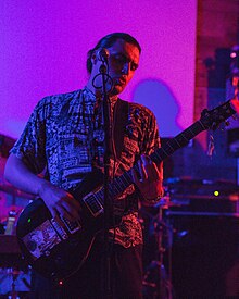 A man standing up, playing guitar during a rock show with his band