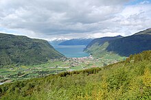 Foto, das auf einem Berg aufgenommen wurde und den Blick auf ein Tal freigibt, das in einen Fjord übergeht. Am Ufer befindet sich eine Siedlung.