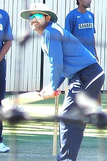 A man in the blue Indian cricket practice kit batting. Other cricketers in the same uniform can be seen standing around