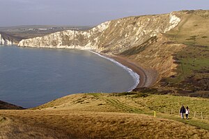 Blick auf die Steilküste in der Worbarrow Bay, aufgenommen von einem Ort mit dem Flurnamen Gold Down. Die Blickrichtung ist in etwa Nordwest. Im oberen Teil des Bildes ganz links ist der Eingang in die Bay of Arish Mell zu sehen. Rechts daneben der Felsen von Cow Corner, wiederum rechts daneben das Kliff des Rings Hill. Oberhalb von Cow Corner, im Bildhintergrund, das Dorf Burngate. Die weißlichen Steilwände bestehen aus Kalksteinen der Oberkreide („Chalk“), das bräunliche Kliff in der rechten Bildmitte besteht überwiegend aus Sandsteinen der Unterkreide („Wealden“).