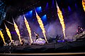 Photo en couleur d'un groupe de musique sur une scène, des flammes brulent au premier plan