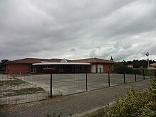 Bâtiment moderne rouge avec auvent et cour en goudron.