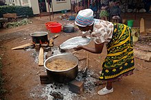 A Tanzanian woman cooks Pilau rice dish wearing traditional Kanga. Pilua for many.jpg