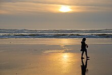 Image of a young girl silhouetted by the setting sun, walking north along the beach.