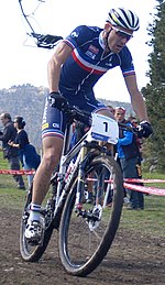 Homme à VTT portant une tenue bleu sombre avec une bande bleu-blanc-rouge sur la poitrine.