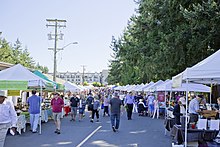 A picture of the farmers market. White tents line a street filled with people.