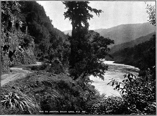 A dirt road next to cliffs and bush-covered hills in the distance, with the Buller River to the right