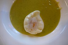 Nahaufnahme eines Suppentellers mit gelbgrüner Suppe, in der ein pochiertes Ei schwimmt