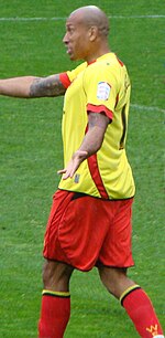 A man wearing yellow shirt and red shorts, standing on a grass field