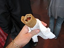 Photographie montrant une main humaine, tenant une saucisse enroulée dans une galette.