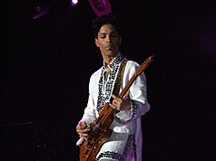 Prince tocando la guitarra con una camisa blanca con pedrería.