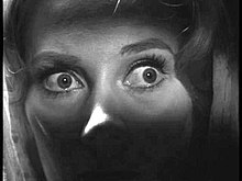 Black and white close up image of a woman's eyes, wide in fear or shock.