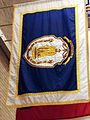 The flag as it appears in the Massachusetts State House Hall of Flags; containing an unusual rendition of The Puritan statue and bearing a different shield and proportions from the previous example.