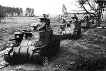 photographie en noir et blanc montrant une colonne de chars sur une route de campagne boueuse.