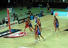 Action de netball où une joueuse, le ballon dans la main, s'apprete à lancer vers le panier.