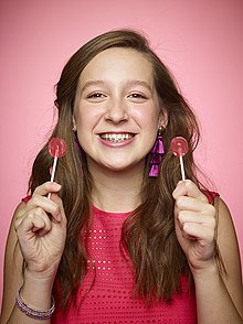 Quarter-length photo of Morse, a teenage girl with braces on her teeth, holding two lollipops