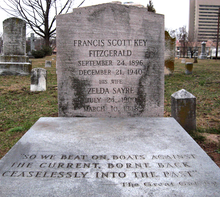 Photograph of the grave of F. Scott and Zelda Fitzgerald in Rockville, Maryland, taken during a snowless winter. The headstone reads: "Francis Scott Key Fitzgerald. September 24, 1896 - December 21, 1940. His wife Zelda Sayre. July 24, 1900 - March 10, 1948." Beneath the headstone is a gray slab inscribed with the final line of The Great Gatsby: "So we beat on, boats against the current, borne back ceaselessly into the past."