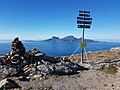 Wegweiser auf dem Keiservarden, im Hintergrund ein Schiff der Hurtigruten vor der Insel Landegode, am Horizont die Silhouette der Lofoten