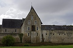 Photographie en couleurs d'anciens bâtiments accolés à un mur d'enceinte, des douves visibles au premier plan.