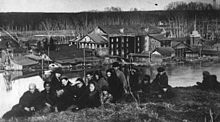 Large group of people on high ground, with buildings and a spring river in the background