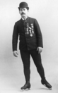 Schwarz-Weiss-Foto von Rubenstein beim Eiskunstlaufen in Orden-behängter Jacke und mit Melone auf dem Kopf.