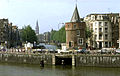 De brug lijkt de verbinding te verzorgen met het water daarachter, de Gelderskade, maar de overspanning loopt in werkelijkheid voor de Schreierstoren langs naar de gracht rechts van het witte hoekhuis