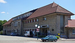 Vue d'un long bâtiment scolaire à étage en pierre et brique, toiture en tuiles.