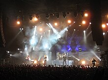 image d'un groupe de rock, composé de cinq membres, jouant devant grand public