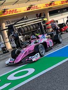 Photographie d'une monoplace de F2 rose et blanche, vue de trois-quarts droit, à l'arrêt, dans la voie des stands.