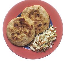 Plat de pupusas assorti de légumes sud américains, sur assiette de terre peinte en rouge sur sa surface intérieure: le centre est peint en bleu.