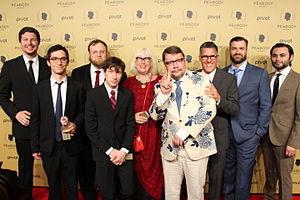 The image depicts a group of adults on the red carpet of an award ceremony.