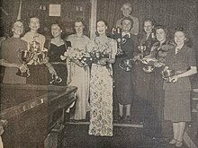Ten women, some holding trophies and flowers