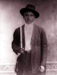 photo sépia d'un jeune noir debout en veste et chapeau