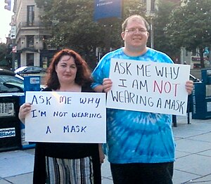 Two Anons hold up signs saying "Ask me wh...