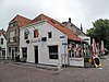 Hoekpand Wal. Afgeknotte lijstgevel, gepleisterd, voor huis met afgewolfd zadeldak. Stoep