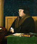 Thomas Cromwell im Mantel und mit Hut, vor einem Schreibtisch sitzend