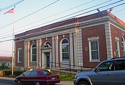Front view of the Haverstraw post office, showing extensive architectural ornamentation, in evening sunlight with two cars parked in front