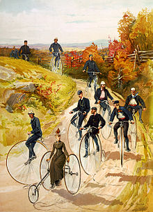 Peinture aux couleurs vives d'une voie vicinale sur laquelle circule un groupe de personnages hissés sur divers modèles anciens de vélocipèdes.
