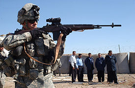Bir ABD askeri, 2006 yılında Irak'taki eğitim sırasında Irak Otoyol Devriyesi (IHP) polis memurlarına M14 tüfeği ateş ederken gösteri yapıyor.