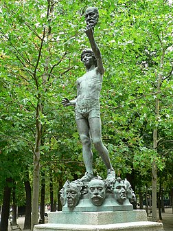 Le marchand de masques (1883, jardin du Luxembourg), sculpture de Zacharie Astruc. De sa main gauche, un jeune marchand brandit le masque de Victor Hugo ; sur le socle de la statue se trouvent ceux des peintres Camille Corot et Delacroix, du sculpteur Carpeaux, des compositeurs Berlioz et Fauré et des écrivains Dumas, Balzac et Barbey d'Aurevilly. (définition réelle 1 536 × 2 048)