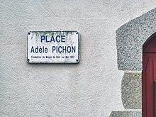 Leicht bemosstes Straßenschild an einer Gebäudewand. Beschriftung Place Adèle Pichon Fondatrice du Musée de Batz sur Mer 1987