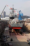 神奈川県横須賀のドライドックおよび米国艦船。ドック内に様々な資材が運び込まれ、フォークリフトなども走り回っている。