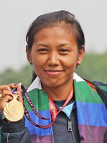 Laishram smiling hard at the camera while holding a medal in her right hand.