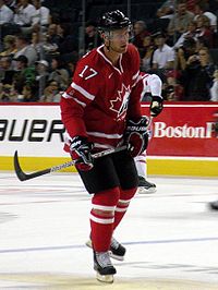Hockey player in red uniform. He holds his stick as if preparing to hit the puck.
