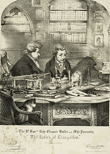An engraved drawing of Eleanor Butler and Sarah Ponsonby, known as the "Ladies of Llangollen". They are shown sitting in a private library wearing smoking jackets, with a cat in the foreground sitting in a chair.
