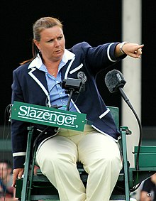 Women in blue blazer sitting on a high green chair with two large microphones in front of her.