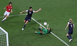 Футбольный матч между Японией и США. Вратарь Хоуп Соло лежит на земле, спасая мяч, а Вамбах рядом с ней.