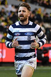 Bearded male athlete wearing long-sleeve guernsey jogging during an Australian rules football game